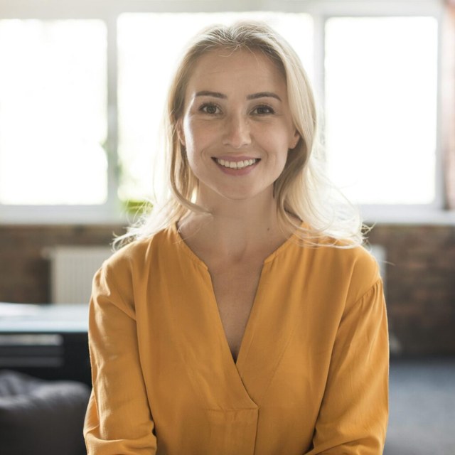A smiling woman with blonde hair wearing a mustard top